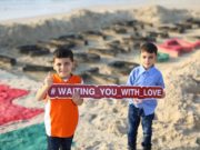 Children on a beach in Gaza with a sign "Waiting you with love".